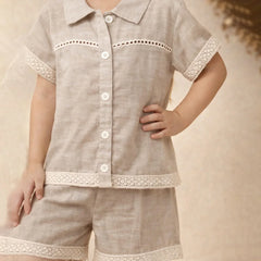 Child wearing a beige outfit with lace details on a neutral background