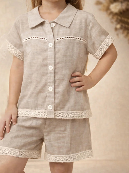 Child wearing a beige outfit with lace details on a neutral background
