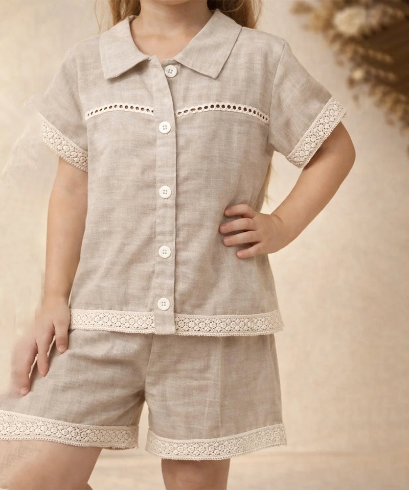 Child wearing a beige outfit with lace details on a neutral background