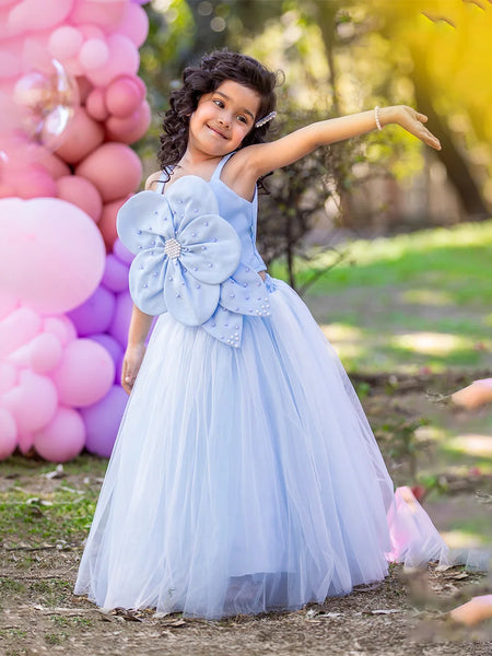 Child in a light blue dress with a large flower detail, standing outdoors with balloons in the background.