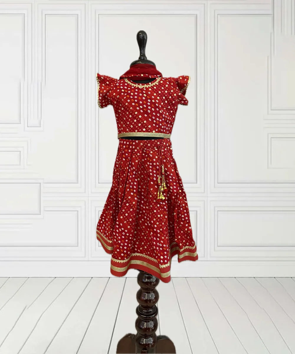 This red coloured bhandej printed kids lehengas consist of a choli that comes with a back closure, a lehenga and a dupatta. It features gota and lace detailing on the choli and lehenga as well as a cute tassel on the lehenga.