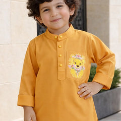 Child wearing a mustard yellow kurta with a lion design on a light stone wall background