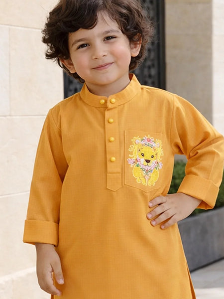 Child wearing a mustard yellow kurta with a lion design on a light stone wall background