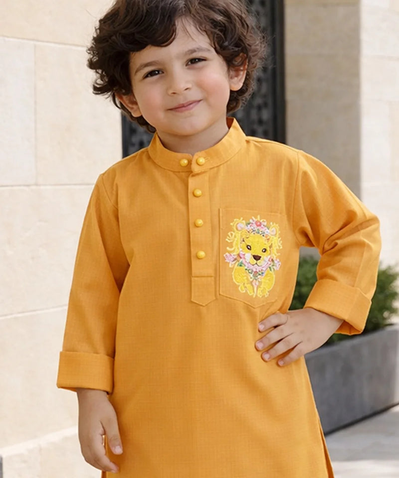 Child wearing a mustard yellow kurta with a lion design on a light stone wall background