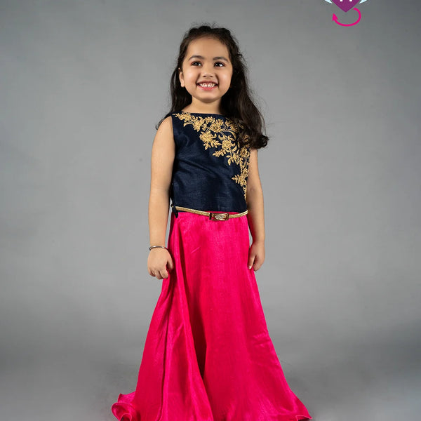 Young girl wearing a black top with gold embroidery and a pink skirt on a gray background