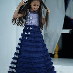Young girl in a blue and silver dress with floral details, posing indoors.