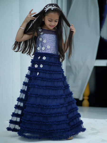 Young girl in a blue and silver dress with floral details, posing indoors.