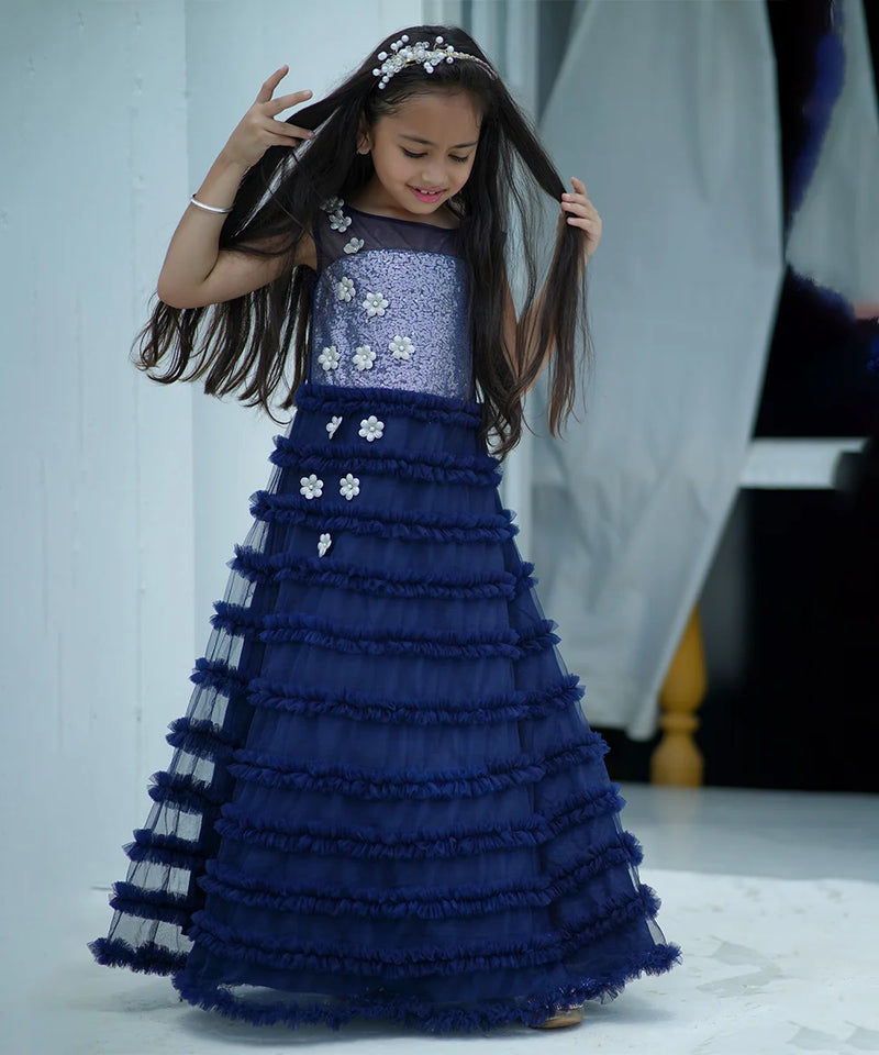 Young girl in a blue and silver dress with floral details, posing indoors.