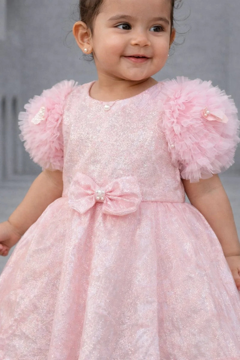 Child wearing a pink dress with ruffled sleeves against a neutral background