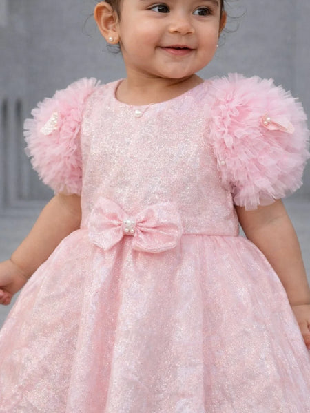 Child wearing a pink dress with ruffled sleeves against a neutral background
