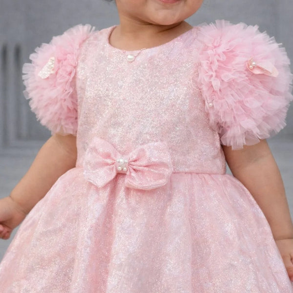 Child wearing a pink dress with ruffled sleeves against a neutral background
