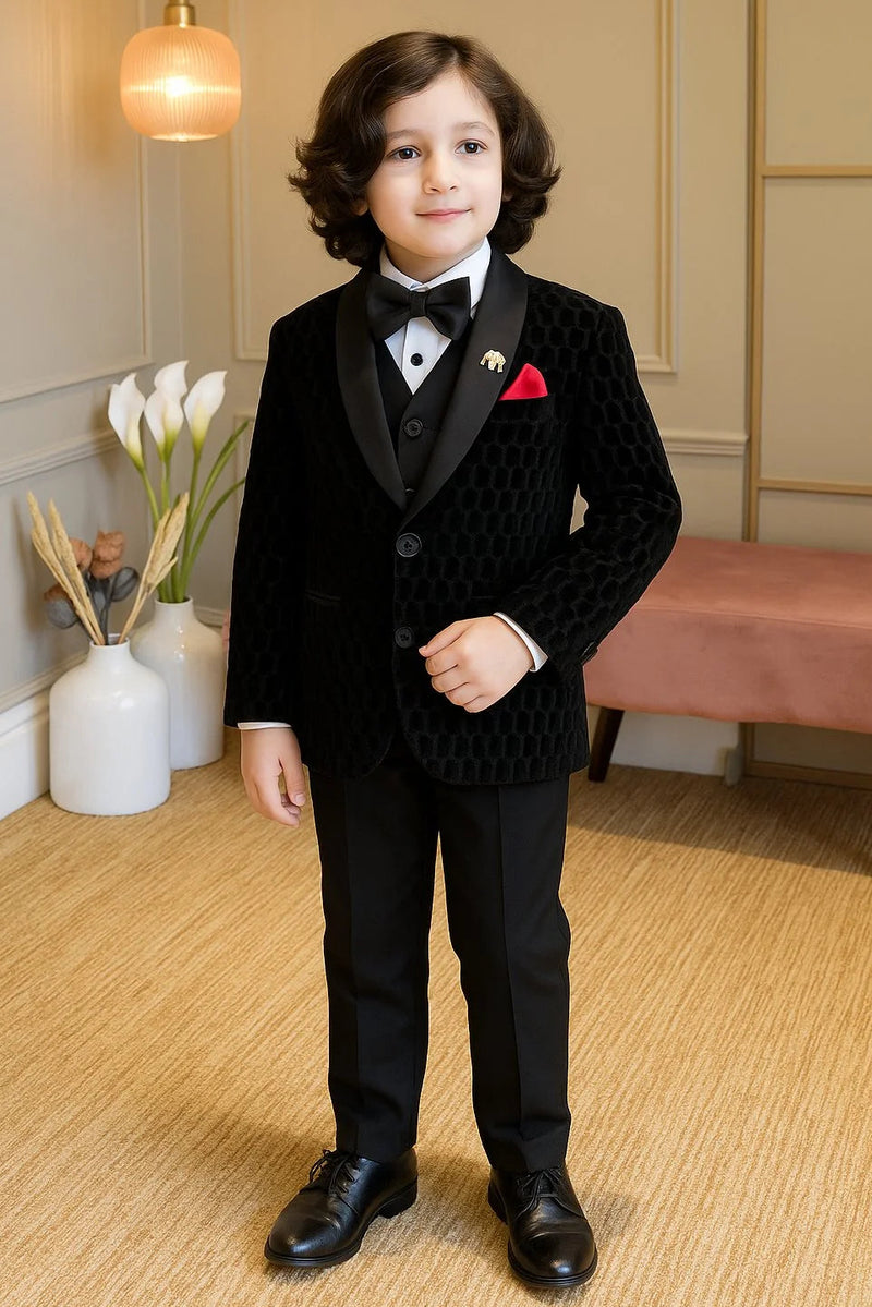 Young boy in a formal black suit standing in a room with decorative elements.