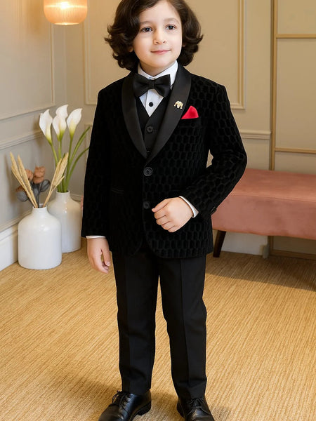 Young boy in a formal black suit standing in a room with decorative elements.