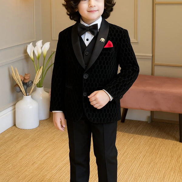 Young boy in a formal black suit standing in a room with decorative elements.