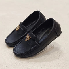 Pair of black loafers with gold accents on a light beige background