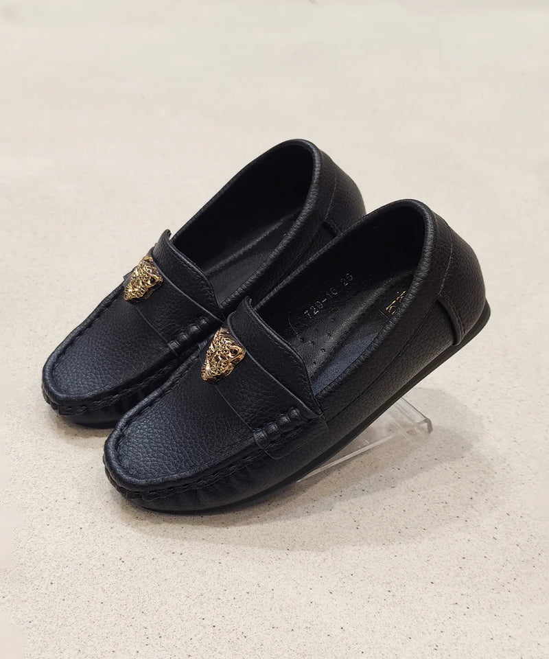 Pair of black loafers with gold accents on a light beige background