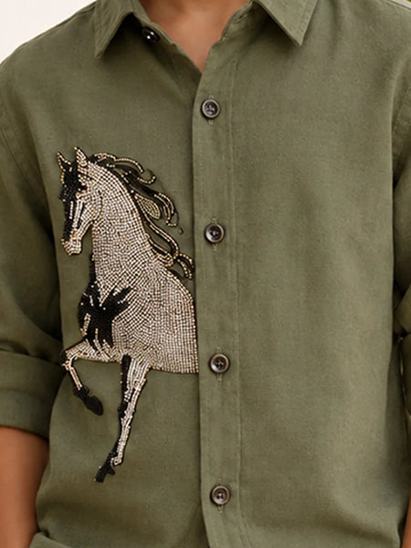 An olive green button-down shirt featuring a large, detailed horse applique embellished with silver and black beads on the left chest, worn by a model.