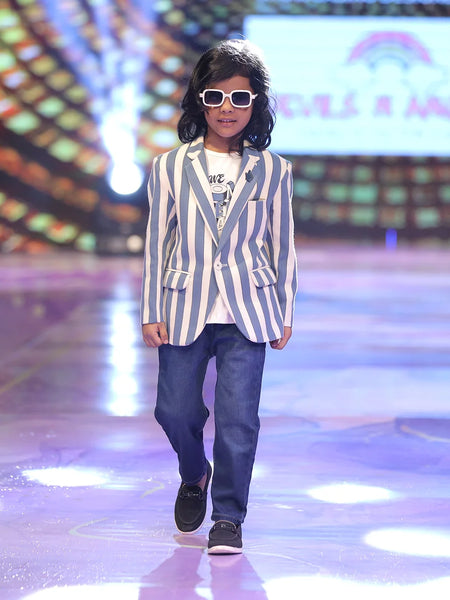Boy walking on a runway wearing a striped blazer and sunglasses, with a colorful background.