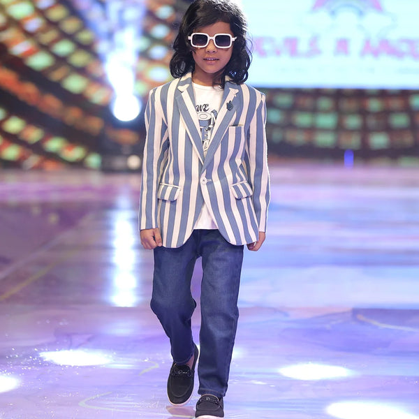 Boy walking on a runway wearing a striped blazer and sunglasses, with a colorful background.