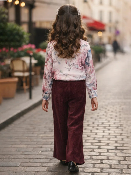 Person wearing a floral blouse and burgundy pants walking on a street.
