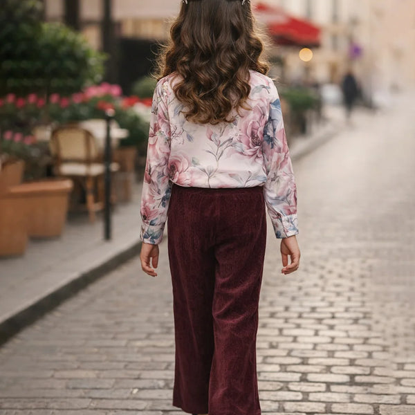 Person wearing a floral blouse and burgundy pants walking on a street.