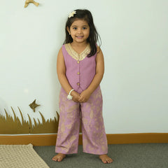 Young girl in a pink outfit standing in a room with a white wall and decorative elements.