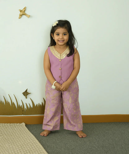 Young girl in a pink outfit standing in a room with a white wall and decorative elements.