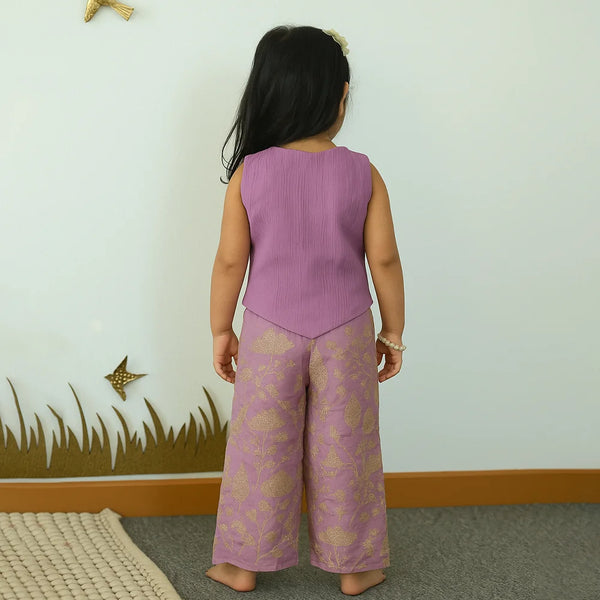 Child wearing a purple outfit with floral patterns in a room with a white wall and decorative elements.