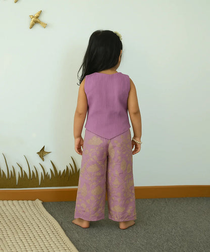 Child wearing a purple outfit with floral patterns in a room with a white wall and decorative elements.