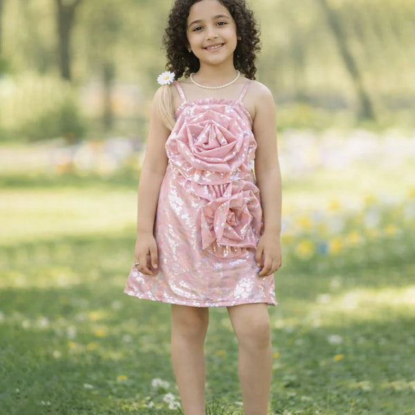 Young girl in a pink dress with floral design standing in a park.