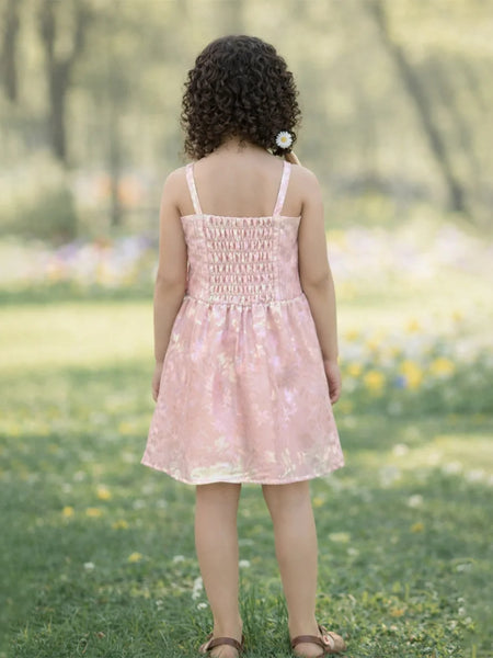 Child in a pink dress standing in a grassy field with flowers.