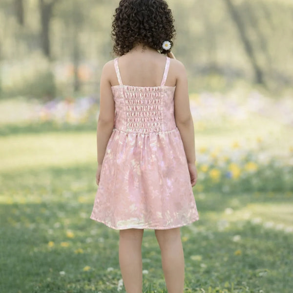 Child in a pink dress standing in a grassy field with flowers.