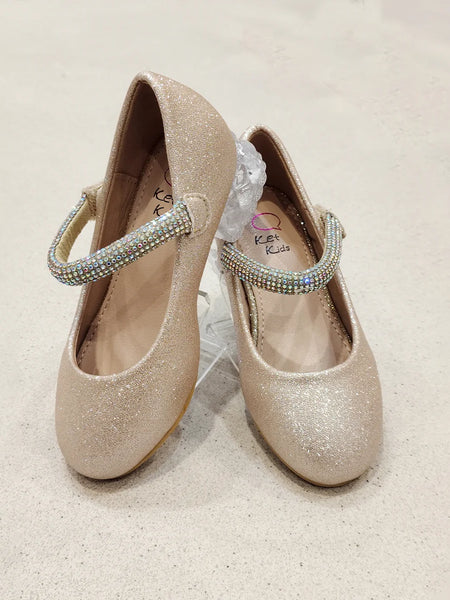 Pair of glittery gold shoes with decorative straps on a light background