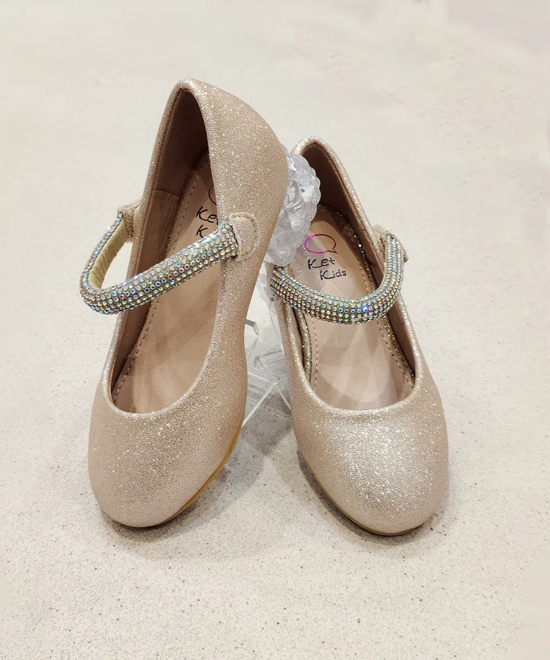 Pair of glittery gold shoes with decorative straps on a light background