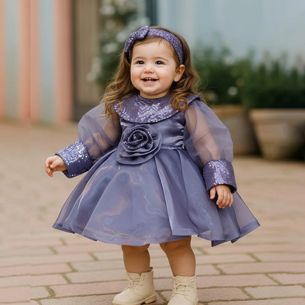 Child wearing a purple dress with a flower detail outdoors on a paved path.