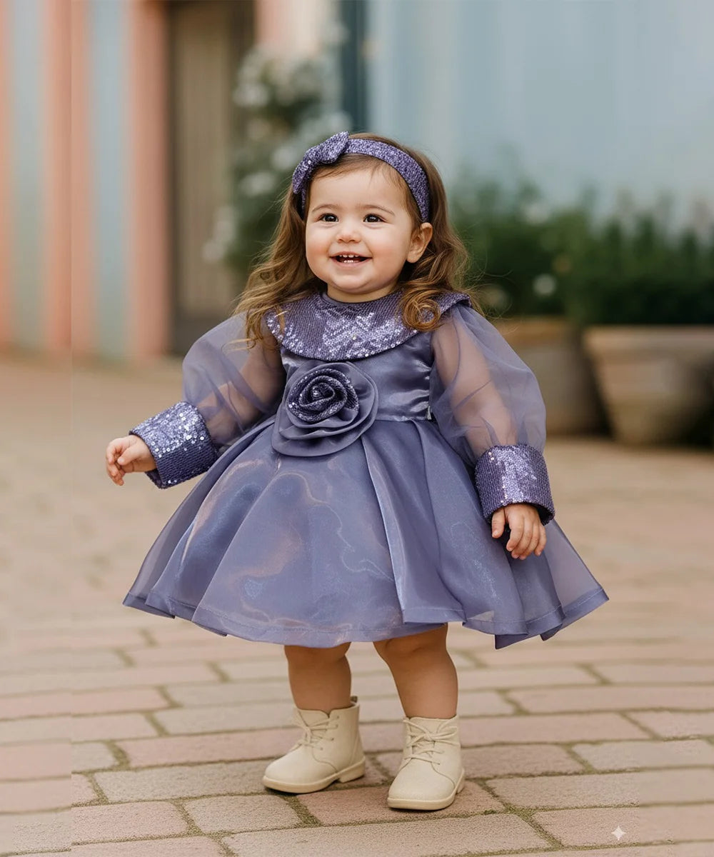 Child wearing a purple dress with a flower detail outdoors on a paved path.