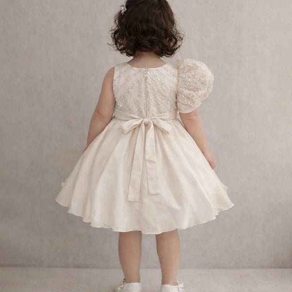 Child wearing a white lace dress with puff sleeves against a plain background