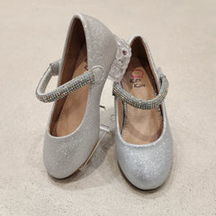 Pair of silver glittery shoes with embellished straps on a beige background