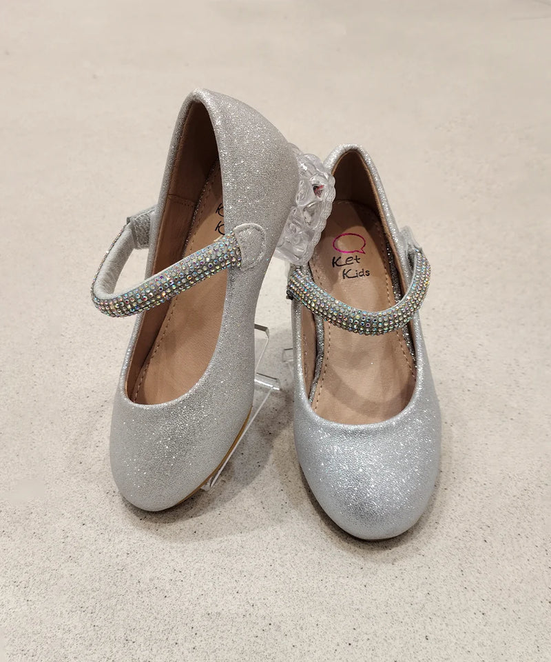 Pair of silver glittery shoes with embellished straps on a beige background
