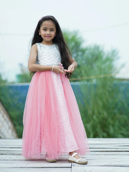 Young girl in a pink and white dress standing outdoors with greenery in the background