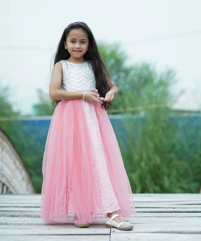 Young girl in a pink and white dress standing outdoors with greenery in the background