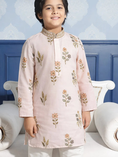 Child wearing a light pink embroidered kurta with white pants against a blue wall.