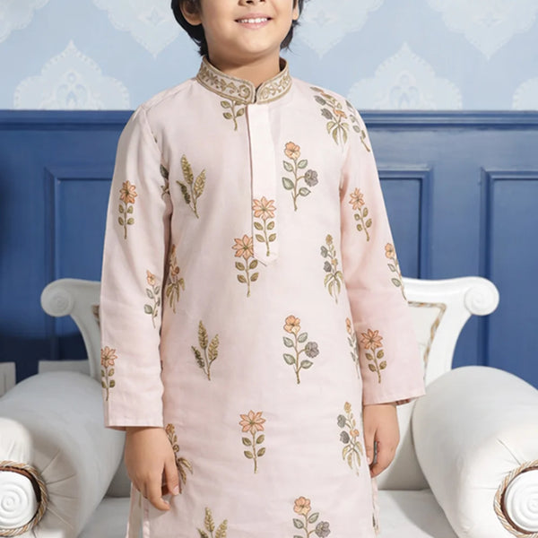 Child wearing a light pink embroidered kurta with white pants against a blue wall.