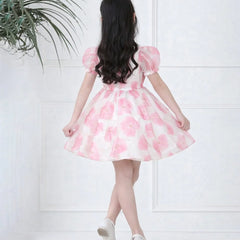 Woman wearing a pink floral dress against a white wall with a plant on the left.