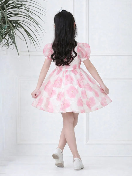 Woman wearing a pink floral dress against a white wall with a plant on the left.