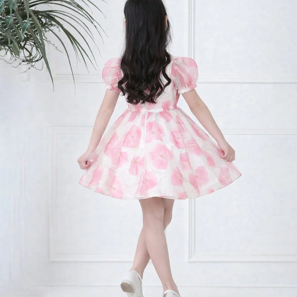 Woman wearing a pink floral dress against a white wall with a plant on the left.