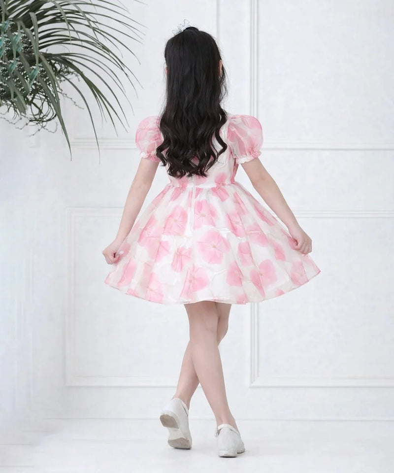 Woman wearing a pink floral dress against a white wall with a plant on the left.