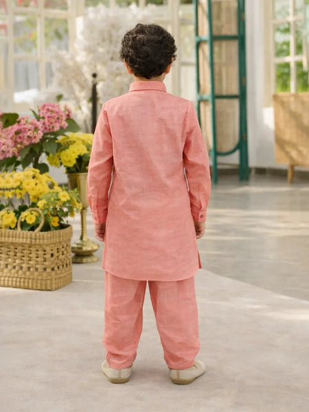 Child wearing a pink traditional outfit standing in a room with flowers and furniture.