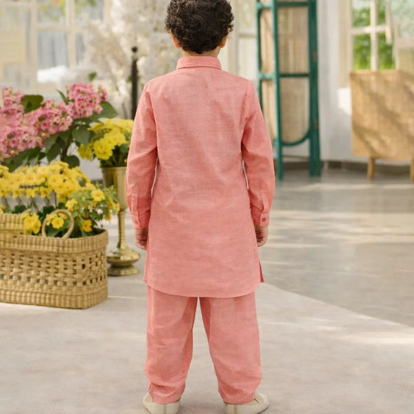 Child wearing a pink traditional outfit standing in a room with flowers and furniture.