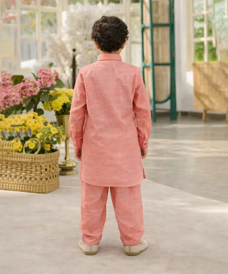 Child wearing a pink traditional outfit standing in a room with flowers and furniture.